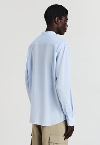 Camicia azzurra a maniche lunghe con tessuto texturizzato, colletto classico e polsini abbottonati, mostrata di schiena, con una vestibilità rilassata.