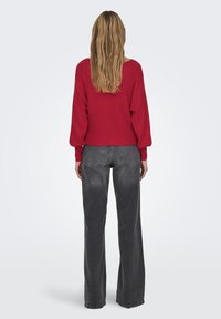 Red ribbed sweater with dropped sleeves, paired with high-waisted, wide-leg black jeans. Smooth fabric with minimal detailing.