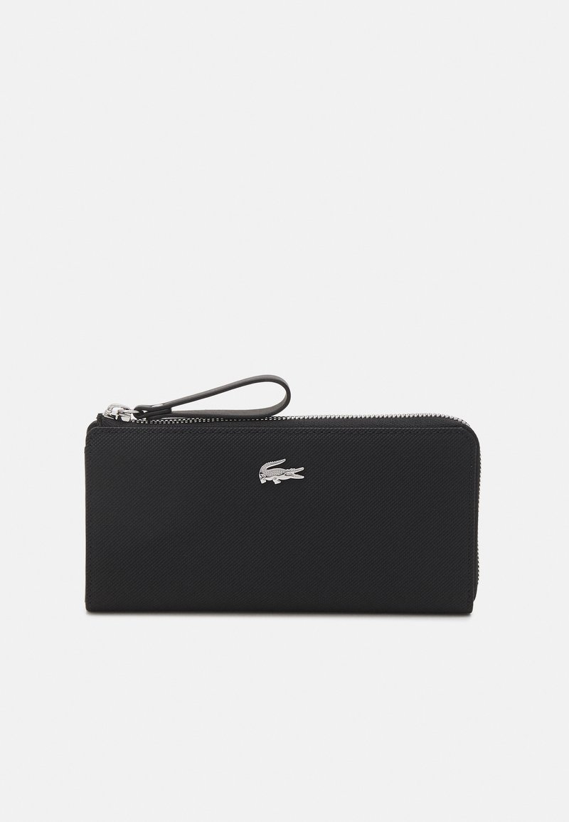 Portefeuille textile noir avec fermeture éclair, arborant un logo Lacoste en argent sur le devant et une sangle de poignet pour un transport pratique.