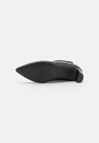 Zapato de cuero negro con punta afilada, parte superior suave y un tacón bajo apilado. La suela es plana y texturizada para mayor agarre.
