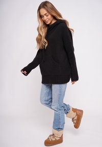 Czarna, teksturowana bluza z kapturem z dużą przednią kieszenią i prążkowanym dołem, zestawiona z jasnoniebieskimi dżinsami i brązowymi butami ocieplanymi futerkiem.