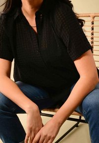 Košile s krátkým rukávem černé barvy s texturovaným vzorem, v kombinaci s tmavě modrými džínami. Košile má límeček a decentní kostkovaný design.