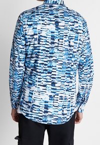 Camicia a maniche lunghe con bottoni in blu e bianco, caratterizzata da un motivo geometrico a pennellate. Tessuto morbido, colletto standard e polsi singoli.