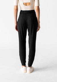 Svarta tapered byxor med en slät textur, hög midja och en ren design. Kombinationen med vita sneakers ger en avslappnad look.