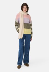 Gebreide trui met horizontale strepen in roze, lavendel, groen en geel. Gepaarde met wijde blauwe jeans en een beige sjaal.