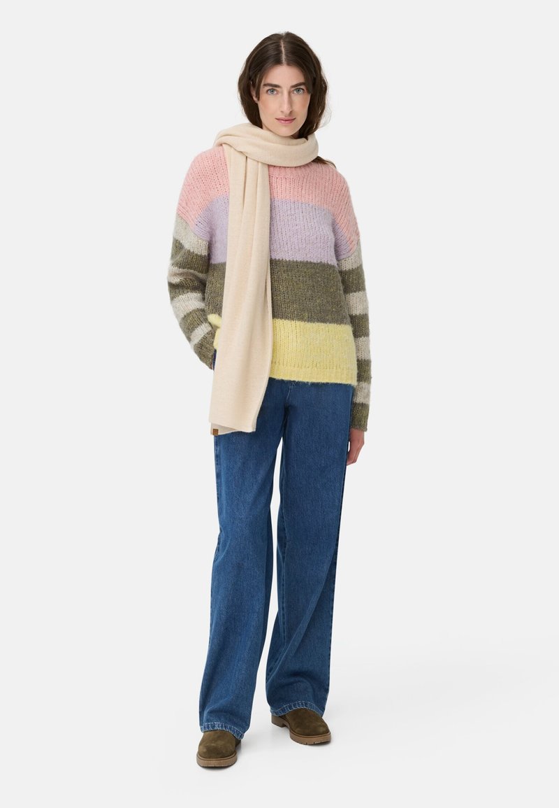Gebreide trui met horizontale strepen in roze, lavendel, groen en geel. Gepaarde met wijde blauwe jeans en een beige sjaal.