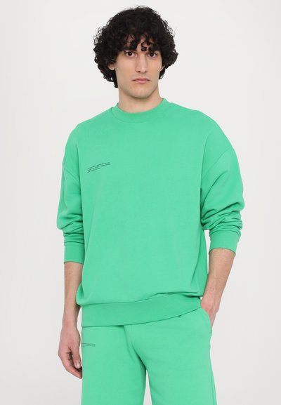 Hanorac verde dintr-un amestec de bumbac, cu guler rotund, mâneci lungi și detalii tipărite în partea stângă sus. Pantaloni de trening în aceeași culoare.