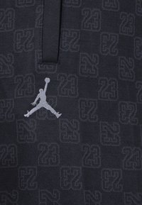 Černá texturovaná tkanina se opakujícím se vzorem "23" s šedým logem Jordan v skákací pozici a malým detailem límce.