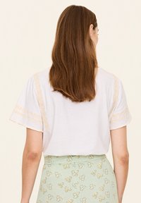 Weißes T-Shirt mit gestickten gelben Akzenten an den Ärmeln, kombiniert mit einem mintgrünen Rock mit floralem Muster.
