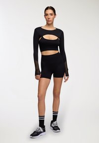 Czarny zestaw sportowy składający się z bluzki z długim rękawem z wycięciami i meshowymi akcentami, w połączeniu z szortami o wysokim stanie oraz czarnymi trampkami.