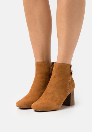 Bottines en daim beige avec un détail tressé, une fermeture éclair sur le côté inclinée et un talon en bois empilé. Bout pointu et texture lisse.
