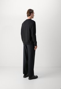 Black sweatshirt with a crew neck, featuring long sleeves and ribbed cuffs. Paired with loose-fitting black trousers and black shoes.