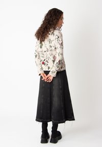 Heled roosa lilledega mustriga kampsun pika varrukaga, mis on ühendatud pika musta denimihaldjaga, millel on kulunud ääred ja vertikaalsed õmblused.