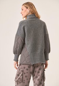 Jersey gris con cuello alto, que presenta una parte superior de punto y una sección inferior acolchada; combinado con pantalones cargo estampados. Costuras detalladas visibles.