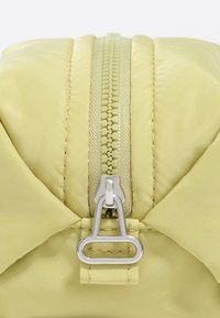 Bolsa con cierre en nylon amarillo claro de textura suave, con un tirador de cremallera plateado y costuras intrincadas a lo largo de los bordes.