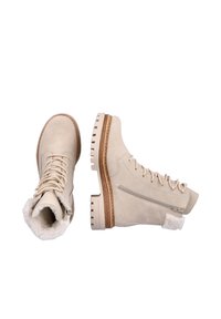 Bottines en daim beige avec finition texturée, devant à lacets, fermeture éclair sur le côté, et semelle à crampons en caoutchouc. Comprend une bordure en fourrure au col et un accent sur le côté.