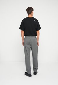 Black cotton t-shirt with a small logo on the back, paired with gray trousers featuring multiple pockets and a relaxed fit. Black shoes.
