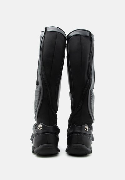 Ψηλά μαύρα αθλητικά μποτάκια με πλευρικά φερμουάρ, υφασμάτινες επιφάνειες και λογότυπο κοντά στις φτέρνες, εμφανίζονται από πίσω σε λευκό φόντο.