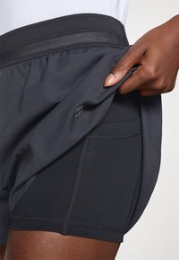 Pantalones cortos deportivos negros con una amplia cinturilla elástica con detalles de malla, bolsillo lateral y una textura de tela suave. Logo mostrado en el dobladillo.