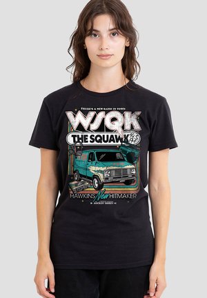 Woman wearing a black T-shirt with a vintage teal radio van, headphones, cassette tape, and "WSQK The Squawk" text design.