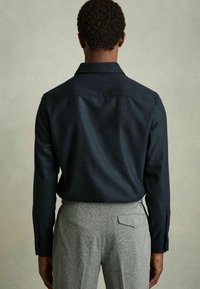 Donkerblauw knoopshirt met een neklap, lange mouwen en een gladde textuur, gecombineerd met lichtgrijze geblokte broek.