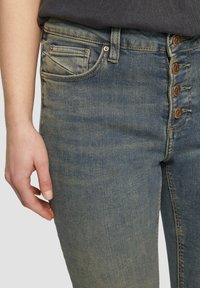 Jean en denim bleu clair avec une taille haute, présentant une fermeture à cinq boutons à l'avant, un léger délavage et des poches latérales.