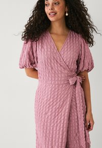 Wickelkleid in sanftem Pink, aus strukturiertem Stoff mit einem gekräuselten Muster. Mit Puffärmeln und einem gebundenen Taillendetail.