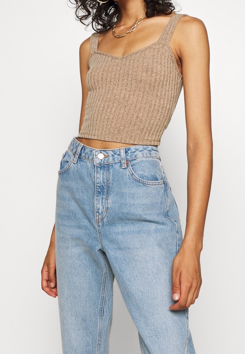 Hnědý žebrovaný pletený crop top s širokými ramínky, zkombinovaný s bledě modrými džíny s rovnými nohavicemi a vysokým pasem. Jednoduchý design a strukturovaná tkanina.