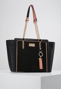 Mustat kangaskassit, joissa on tekstuuripaneelit, vaaleanpunainen reuna, kultaketjuhihnat ja koristelu, jossa on kultainen ja vaaleanpunainen nahkaketju roikkumassa yhdestä hihnasta.