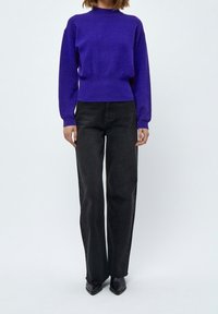 Jersey de punto morado con un cuello alto, puños acanalados y una cintura ajustada, combinado con unos vaqueros negros de pierna recta de tiro alto y zapatos negros de punta.
