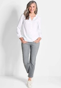 Weiße Bluse mit Knopfleiste, langen Ärmeln und grauen Jeans. Strukturierter Stoff, lockere Passform, kombiniert mit weißen Sneakers.