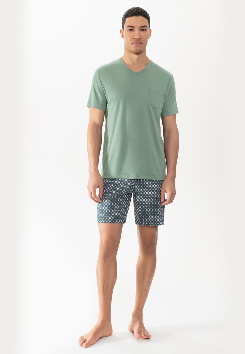Green v-neck t-shirt with a chest pocket paired with patterned shorts featuring a blue background and small white geometric designs.