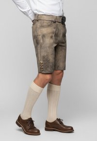 Kniejne, beżowe lederhosen z misternym haftem, pięć brązowych guzików z boku, w połączeniu z kremowymi skarpetkami do kolan i brązowymi butami.