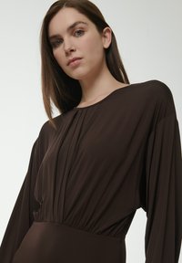 Braunes, langärmliges Kleid aus einem weichen, leichten Material mit einem gefältelten Design am Ausschnitt und einem taillierten Bund.