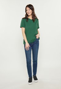 Grön kortärmad t-shirt med V-ringning, i kombination med åtsittande blå jeans och svarta sneakers med vita sulor. Enkel design, mjuk textur.