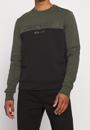 Grön och svart sweatshirt med rund hals, långa ärmar och Calvin Klein-logotyp i text över bröstet. Mjuk bomullsblandning.