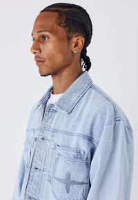 Giacca di denim azzurro chiaro con un design classico, caratterizzata da una chiusura frontale con bottoni, molteplici tasche e un delicato dettaglio ricamato a forma di stella.