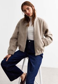 Beige fleec bomberjacka med dragkedja fram, ribbade ärmslut och rund halsringning. Matchad med högmidjade mörka denimjeans.