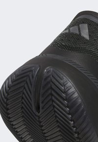 Baskets de sport noires avec une tige texturée, une semelle arrondie dotée d'un motif de crampons en zigzag, et un logo discret sur le côté.