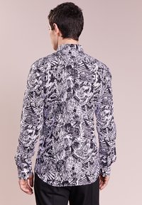 Long-sleeve shirt in black and white with abstract patterns, featuring a pointed collar and buttoned cuffs. Made of smooth fabric.