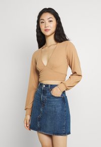 Top cropped de manga longa em ribana bege com um profundo decote em V, combinado com uma saia A-line em denim azul. Ambas as peças apresentam designs minimalistas.