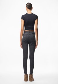 Μαύρο κοντό μπλουζάκι συνδυασμένο με σκούρες γκρι στενές τζιν. Τα τζιν διαθέτουν κλασικό σχέδιο πέντε τσεπών και μια διακριτική υφή. Καφέ μποτάκια μέχρι τον αστράγαλο ολοκληρώνουν την εμφάνιση.