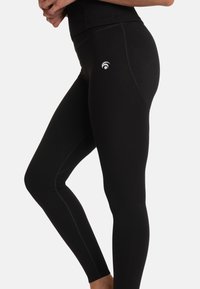 Zwarte leggings van rekbaar materiaal, ontworpen voor comfort met een aansluitende pasvorm. Bevat een wit logo nabij de taille en contrasterende stiksels.