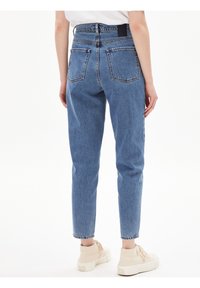 Jeans de tiro alto en azul claro con pierna recta y dos bolsillos traseros. Presentan costuras visibles y una etiqueta de marca negra en la cinturilla.