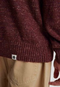 Bordeaux gebreide trui van textiel met een geribbelde zoom en een klein merklabel; gecombineerd met lichtbeige broek, wat casual kleding toont.