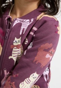 Paars ritsjack met speelse kattenpatronen in verschillende kleuren, gemaakt van zachte stof met een geribde kraag en manchetten.