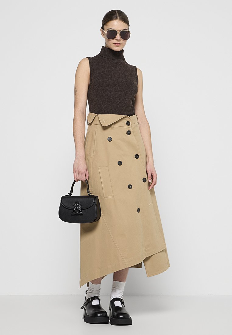 Beige Trenchcoat mit asymmetrischem Saum und doppelreihigen Knöpfen, kombiniert mit einem braunen ärmellosen Oberteil und einer schwarzen Handtasche, akzentuiert durch runde Sonnenbrillen.