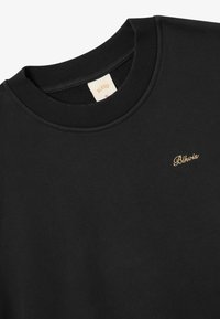 Schwarzer Pullover mit geripptem Rundhalsausschnitt, ausgestattet mit einem dezenten, goldenen, gestickten Logo. Glatte Textur, minimalistisches Design, keine Muster.