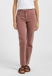 Jeans de talle alto y corte ajustado en rosa empolvado, con cinco bolsillos, cremallera y detalles de costura sutiles. Combinados con sandalias de tiras.