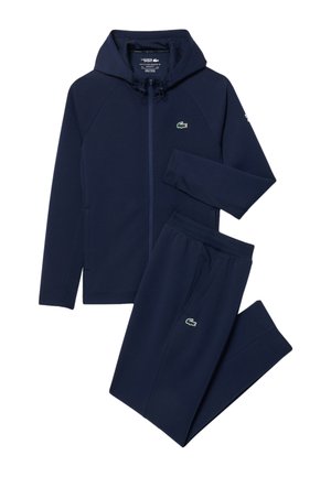 Marineblauwe hoodie met rits en bijpassende joggingbroek met groen krokodillenlogo op borst en dij, plat liggend op een witte achtergrond.